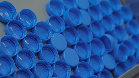 Close up: many blue plastic bottle caps moving on conveyor belt of compression molding machine at factory, exhibition: production line. Manufacturing, industry, recycling, technology equipment concept