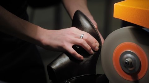 Close up: shoemaker, shoes master using automatic orange shoe polish machine tool for polishing black leather women footwear at workshop