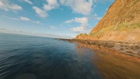 Flying Over Rocky Coastline alongside Cliffside with Blue North Atlantic Ocean Water Towards the Sun During Sunrise. Bird Eye View 4K Cinematic Drone Footage. Soar Above Sea Coast From Up in the Air