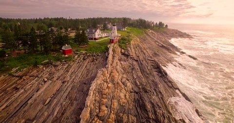 An establishing aerial shot of the Pemaquid Point Lighthouse in Maine at sunrise.