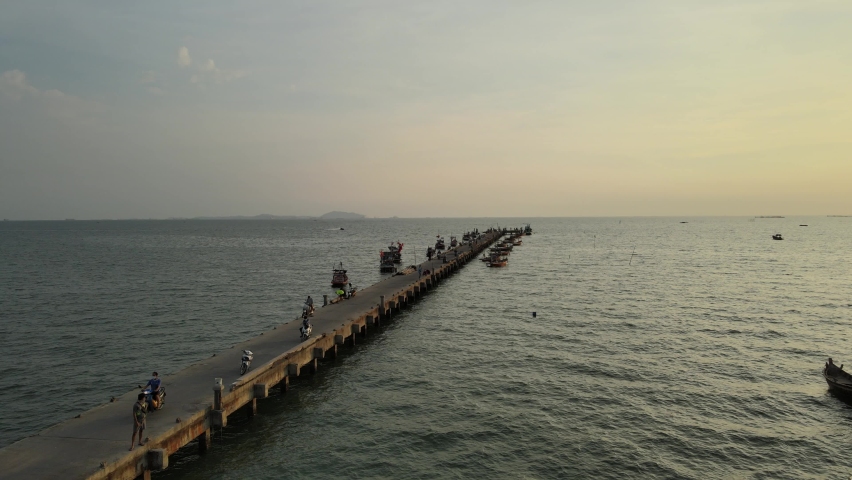 Aerial drone view of people walking on the pier against the sunset. Local people are fishing, tourists are walking before going to bed. Chonburi, Thailand.