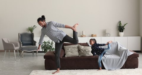 Active African family sporting indoor. Young father and little cute daughter standing barefoot on carpet perform balancing exercise in living room. Work out training at home for health, hobby concept