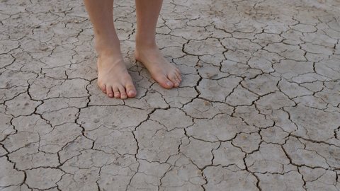 Cracked soil. Close-up of a foot of an adult walking barefoot along the bottom of a dried-up lake or river, stepping on cracked soil destroyed by erosion - a concept of environmental issues. 4K