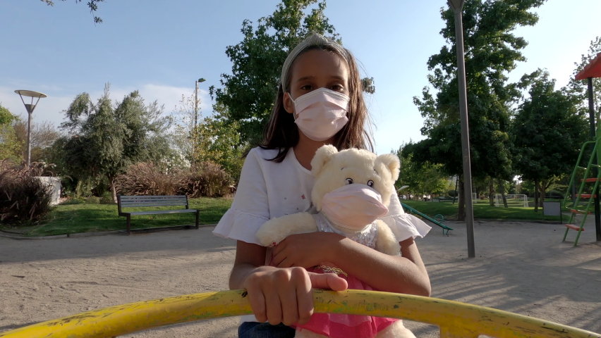 little Latin American girl and her bear with mask rolling in toy public park