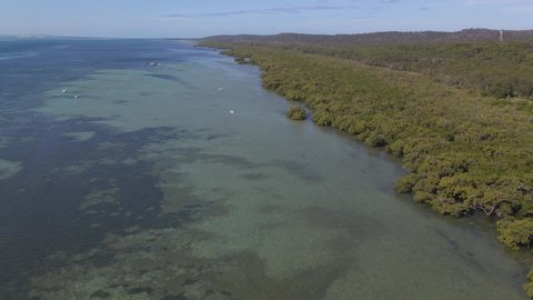 Boats Floating On Calm Water Of Coral Sea With Lush Green Forest - North Stradbroke Island, Minjerribah, Queensland, Australia. - aerial