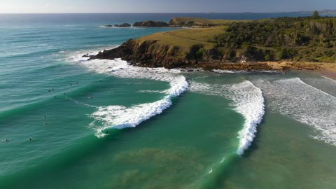 Rotating drone shot of surfers in ocean revealing Coffs Harbour Australia