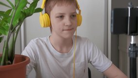 Boy blogger in yellow headphones talking with followers. Teenager live streaming actively gesticulating in front of smartphone screen