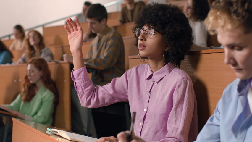 Group of students learns at lecture room. Young people study in university or pupil sitting at school lesson. Teen raises hand and asks teacher at auditorium. Modern education indoors of college hall | Shutterstock HD Video #1072141856