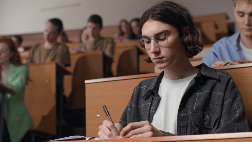 Group of students learns at lecture room. Young people study in university or pupil sitting at school lesson. Teen listens to teacher and writes at auditorium. Modern education indoors of college hall Royalty-Free Stock Footage #1072141868