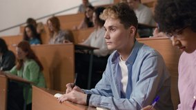 Group of students learns at lecture room. Young people study in university or pupil sitting at school lesson. Teens listen to teacher and write at auditorium. Modern education indoors of college hall - Powered by Shutterstock - Get 15% off with code: PIKWIZARD15