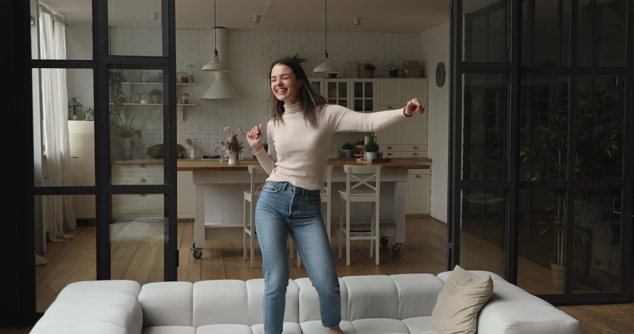 Carefree young vivacious woman dancing alone barefoot on sofa in modern living room at home. Happy female celebrate moving relocation day enjoy new rented apartment. Stress-free weekend, fun concept Royalty-Free Stock Footage #1072143227