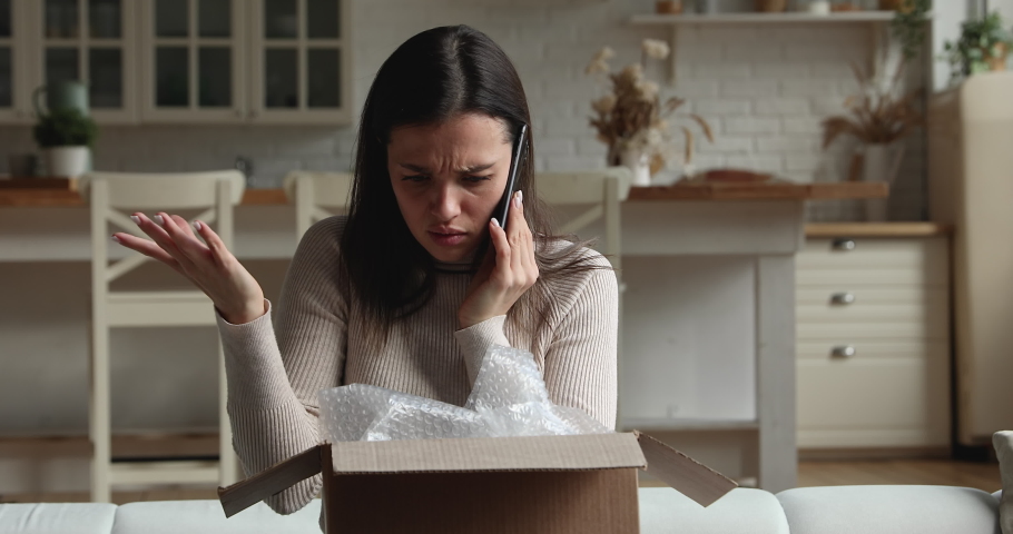 Dissatisfied young woman sit on sofa open parcel box looks inside check purchased delivered damaged items feels upset. Client of postal delivery services calls to customer support express complaints | Shutterstock HD Video #1072143236