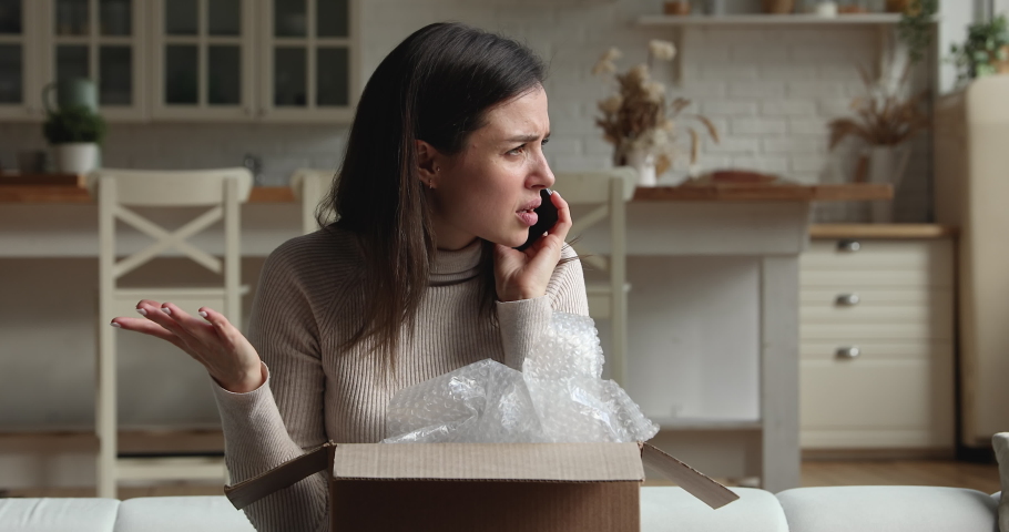 Dissatisfied young woman sit on sofa open parcel box looks inside check purchased delivered damaged items feels upset. Client of postal delivery services calls to customer support express complaints Royalty-Free Stock Footage #1072143236