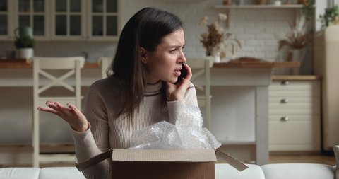 Dissatisfied young woman sit on sofa open parcel box looks inside check purchased delivered damaged items feels upset. Client of postal delivery services calls to customer support express complaints