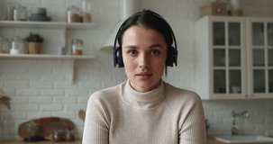 Head shot portrait lively young woman wear wireless headphones lead videoconference conversation. Streaming activity, vlogging, share news to friend using video call application, modern tech concept