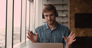 Young businessman sit at workplace in modern office wear wireless headphones talking lead business negotiation with corporate client use laptop and videoconference application, videocall event concept