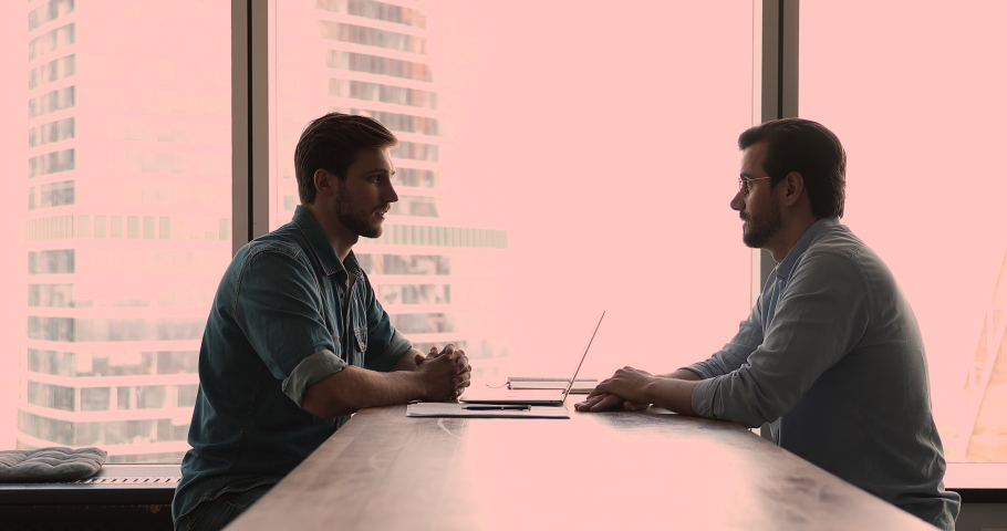 In modern office two millennial man sit at table in front of each other, HR manager lead job interview talk to vacancy applicant. Business negotiation between client and company representative concept Royalty-Free Stock Footage #1072143623