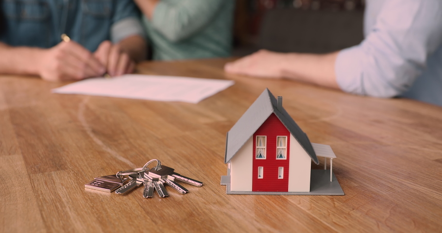 Bunch of keys and cottage house toy model on wooden table close up view, couple sign bank loan agreement or real estate rental contract, closing deal with handshake on background. Buy property concept Royalty-Free Stock Footage #1072143659