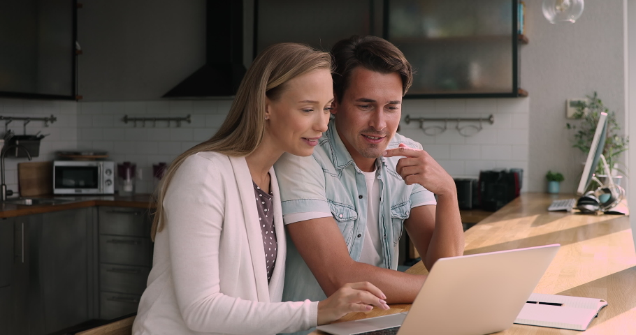 Young married couple sit in kitchen use laptop receiving commercial offer feel happy celebrate lucky moment. Online auction lottery win, job opportunity, last minute tour chance got, good news concept Royalty-Free Stock Footage #1072143686