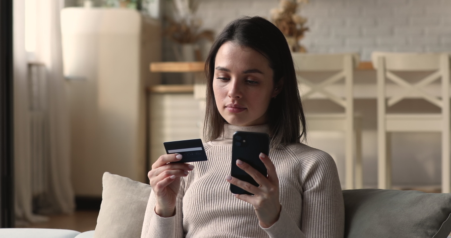 Woman sit on sofa hold credit card use phone try to pay through e-bank app experiences problems due insufficient funds, no money, insecure online payment, scam, fraud, unsuccessful transaction concept Royalty-Free Stock Footage #1072143749