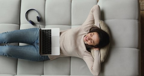 Top view serene woman accomplish work on laptop put hands behind head relaxed on sofa, distracted from internet activity, breath fresh air reduces fatigue. Stress-free, pause, rest, daydreams concept