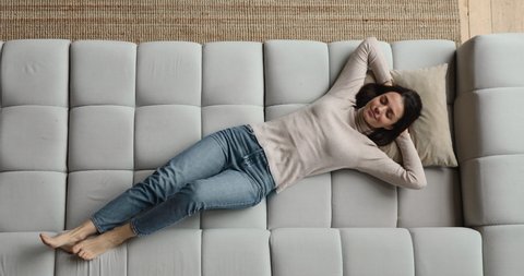 Full length top view blissful woman put hands behind head lying on cushion resting on comfy sofa breath fresh air daydreams enjoy stress-free weekend at modern flat. Relaxation, visualization concept