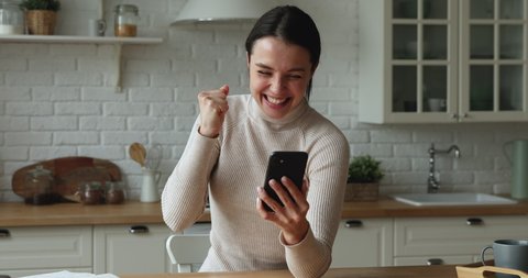 Beautiful young woman sit in kitchen hold smart phone received sms read great news about hiring, sales growth, lottery win, express candid emotion, sincere feelings celebrate moment of victory concept