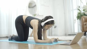 Asian women athletes wear black sportswear, white headphones, plank stretch, legs, arms up yoga, practice watching laptop classes online at home during a New-normal lifestyle.