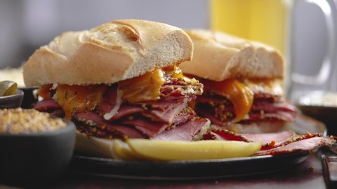 Delicious pastrami meat sandwiches served with glass of beer, pickles, potato chips and sides.