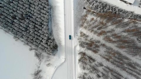 Aerial Top View Drone footage in Hokkaido Japan while snowing above the white road that blue car drive along