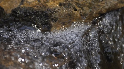 A stream of clear water with a fast current flows under the stone and bubble with small bubbles. Spring flood. Close-up of a stream. Fresh water stream. Melted water.