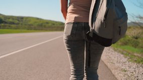 A woman with a backpack walks along the road. Rear view. Moving the camera down. The concept of hitchhiking trips