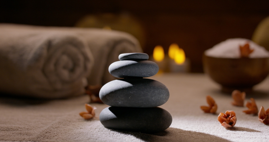 Spa salon equipment. Close up shot of massage hot stones with little flowers around and towels with flaming candles on background - wellness, spa concept 4k footage | Shutterstock HD Video #1072161494