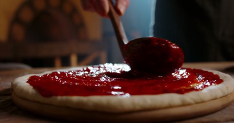 Close up shot of applying tomato sauce on pizza dough. Italian chef cooking pizza in restaurant kitchen. Food and drink, food art 4k footage