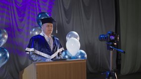 adult male rector of institute conducts ceremonial part of presentation of diploma to students using video link due to quarantine and pandemic backdrop of balloons