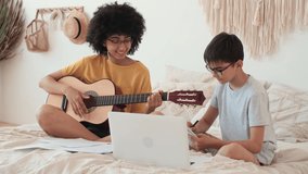 Music Teaching, Musical Education, Playing Guitar, Time Together. African American Woman teaches boy to play guitar using laptop.