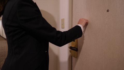 Woman knock in door of hotel room, but nobody answer, she try again. Typical lodging corridor, closed door and lady in black suit stand against, half length shot