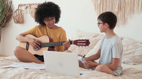 Music Teaching, Musical Education, Playing Guitar, Time Together. Woman teaches boy to play guitar using laptop.