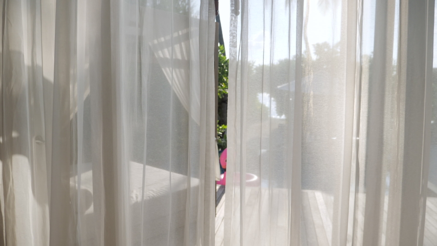 Young woman pulls hotel room curtains and walks outside. Female opens window curtains and walks on pool deck. People checking in hotel 