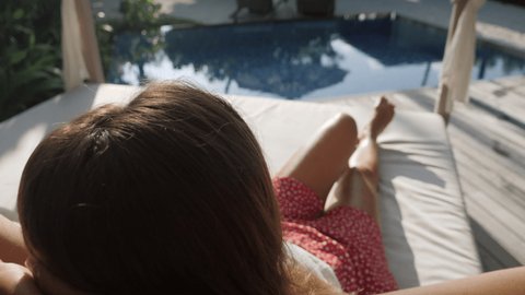 Slow motion: Young woman relaxing by the pool in her private beach villa. Female living luxury lifestyle in a beach resort surrounded by lush green garden 