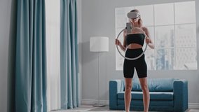 Young woman in black sportswear trains with contemporary virtual reality headset holding ring with fixed phone in room slow motion