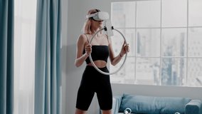 Slim blonde lady with virtual reality headset does squats putting up frame shooting blog with mobile phone in living room slow motion