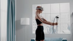 Attractive woman blogger in black sportswear raises knees training with VR goggles and phone fixed on ring in room slow motion