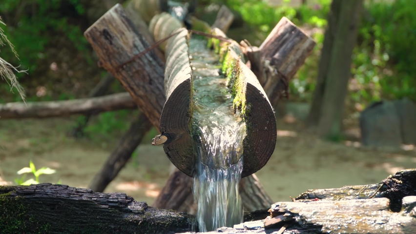 Clear fresh water flowing through open wooden pipes filling wooden water mill for milling wheat and rice in Korean folk village Yongin City, Korea