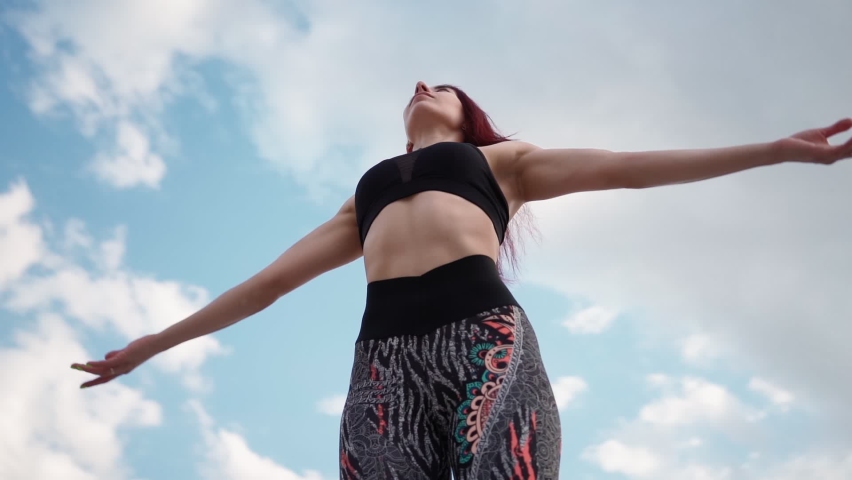 Athletic Woman with Beautiful Figure in Tank Top Raises Her Hands Up Feeling Freedom. Slim Girl in Sportswear Stands on Background Stunning Sky with Her Arms Up. Camera Rotates 360 Degrees Slow Motion Royalty-Free Stock Footage #1072179209