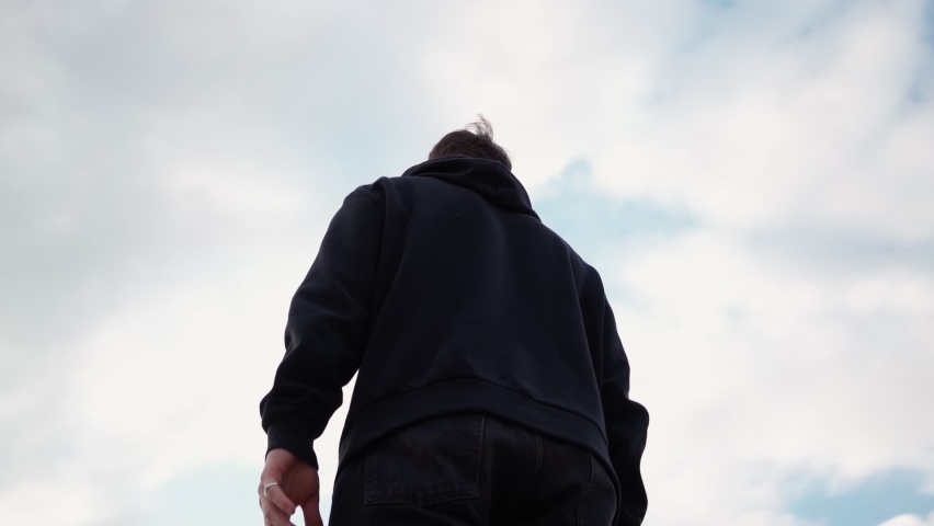 Happy Man in Black Hoodie Raises His Hands Up, Rejoicing in Success and Victory Against Background Beautiful Sky. Guy Experiences Sense Freedom and Well-being. Camera Rotates 360 Degrees. Slow Motion. Royalty-Free Stock Footage #1072179212