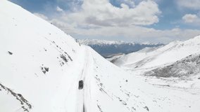 Aerial top view from drone of a camper vehicle driving on snowy ice road with a beautiful mountain landscape.Camper vehicle climbing ladakh.