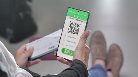 Hand holding covid-19 green card vaccination passport on smart phone screen,woman sits at the airport departure area checking health certificate and boarding pass