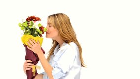 Cute blond woman smelling a bunch of flowers against a white background