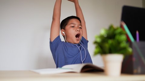 slow motion scene on asian kid boy stretching body and yawing while studying online on school e-learning webinar program in house for homeschool technology lifestyle concept